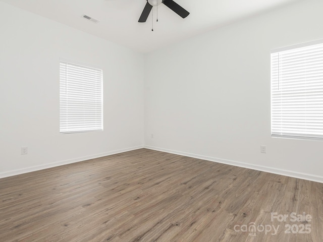 empty room featuring a ceiling fan, visible vents, baseboards, and wood finished floors