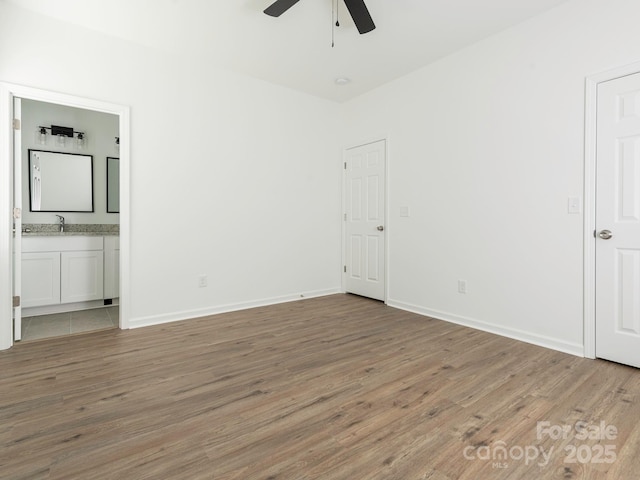 unfurnished bedroom with wood finished floors, ensuite bath, a sink, and baseboards