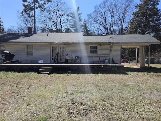 rear view of property with a chimney, an attached carport, roof with shingles, a deck, and a yard