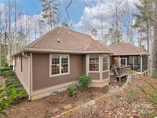 rear view of property with a sunroom, a chimney, a deck, and roof with shingles