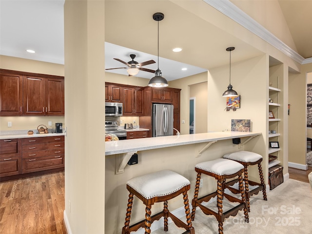 kitchen with appliances with stainless steel finishes, a kitchen breakfast bar, decorative light fixtures, a peninsula, and light countertops