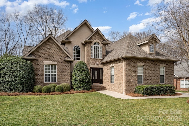 view of front of home featuring stucco siding, brick siding, a front lawn, and roof with shingles