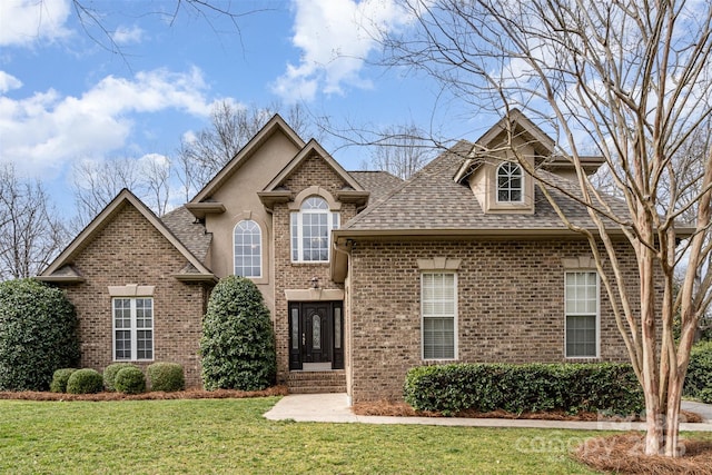 view of front of home with brick siding, stucco siding, a front lawn, and roof with shingles