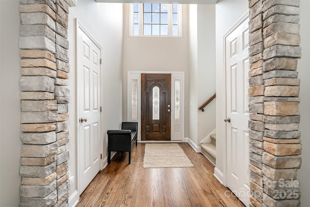 foyer entrance with stairs, a high ceiling, baseboards, and wood finished floors