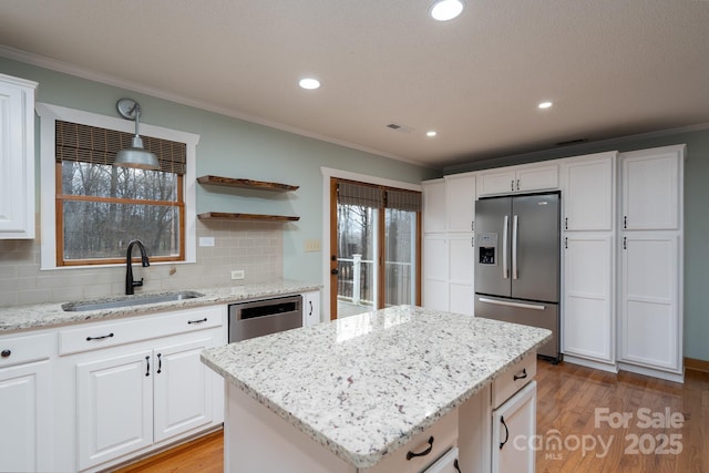 kitchen with crown molding, light wood-style flooring, stainless steel appliances, white cabinetry, and a sink