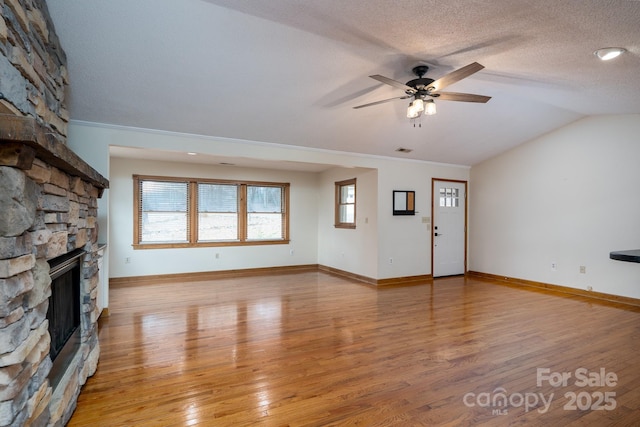 unfurnished living room with a ceiling fan, light wood finished floors, a fireplace, vaulted ceiling, and a textured ceiling