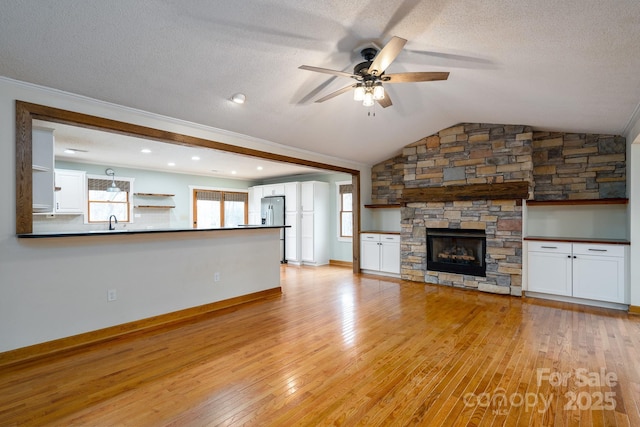 unfurnished living room featuring a ceiling fan, a textured ceiling, light wood-style floors, a stone fireplace, and lofted ceiling