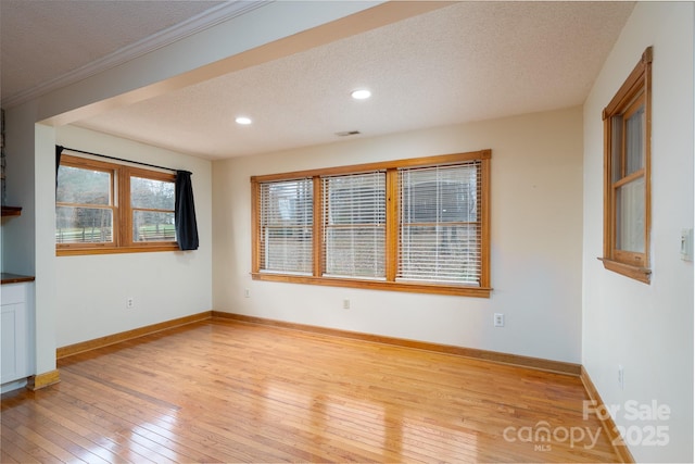 spare room featuring light wood-style flooring, baseboards, and a textured ceiling