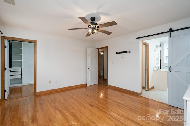 unfurnished bedroom with light wood-type flooring, a barn door, baseboards, and a walk in closet