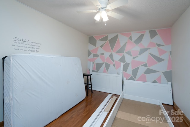 bedroom with wallpapered walls, an accent wall, wood finished floors, a textured ceiling, and a ceiling fan