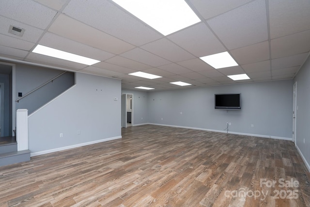 unfurnished living room with wood finished floors, baseboards, and a paneled ceiling