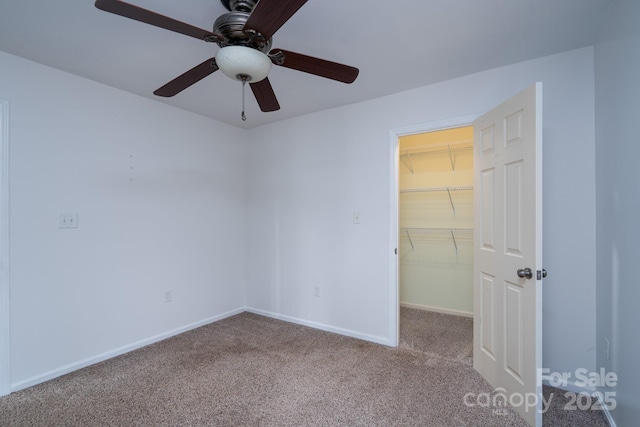 unfurnished bedroom featuring a walk in closet, a closet, carpet, baseboards, and ceiling fan