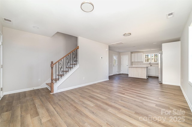 unfurnished living room with baseboards, visible vents, light wood finished floors, and stairs