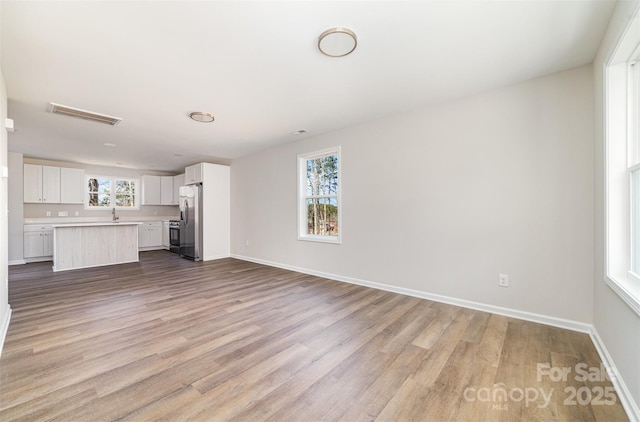 unfurnished living room featuring visible vents, baseboards, and wood finished floors