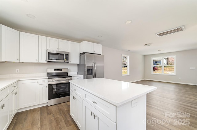 kitchen with stainless steel appliances, wood finished floors, visible vents, and a center island