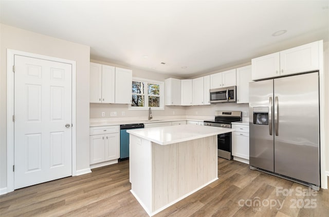 kitchen with light countertops, appliances with stainless steel finishes, wood finished floors, and white cabinets