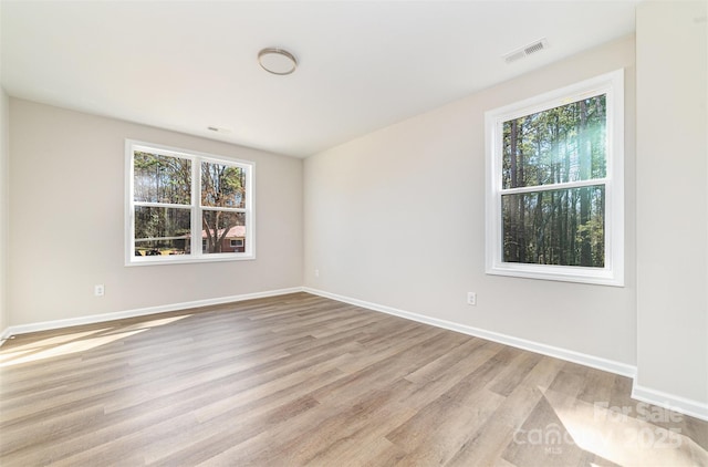 spare room with baseboards, light wood-style flooring, visible vents, and a healthy amount of sunlight