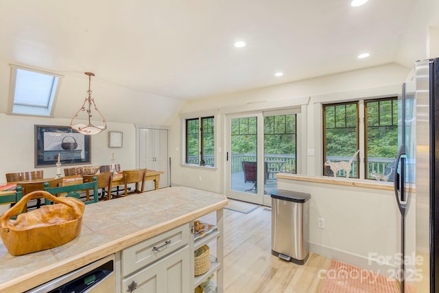 kitchen with stainless steel appliances, tile countertops, lofted ceiling, healthy amount of natural light, and white cabinets