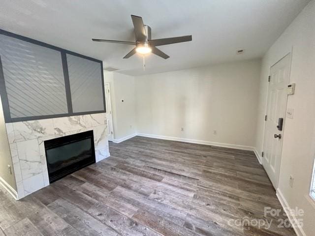 unfurnished living room featuring a premium fireplace, dark wood finished floors, a ceiling fan, and baseboards