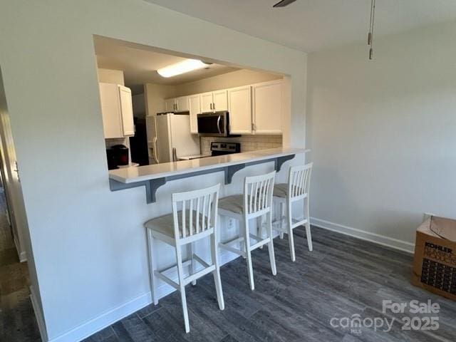 kitchen with white refrigerator with ice dispenser, light countertops, stainless steel microwave, backsplash, and dark wood-type flooring