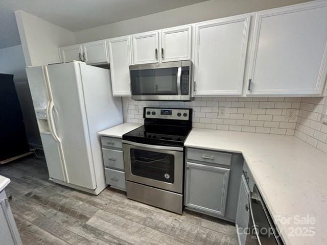 kitchen featuring light wood finished floors, stainless steel appliances, light countertops, backsplash, and gray cabinetry