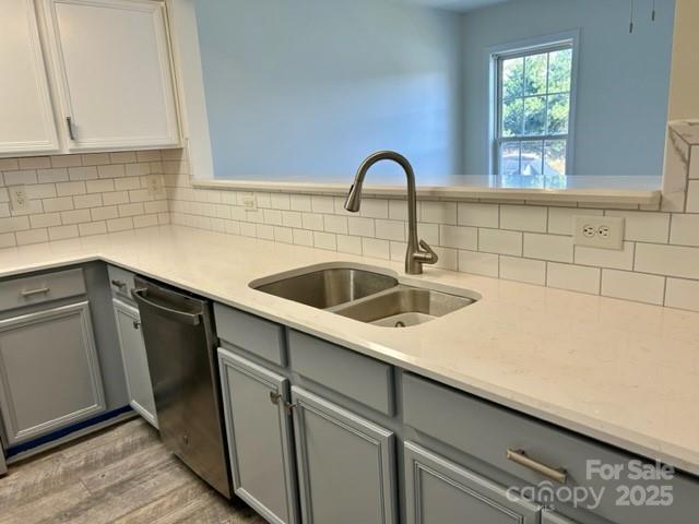 kitchen with tasteful backsplash, light countertops, stainless steel dishwasher, gray cabinetry, and a sink