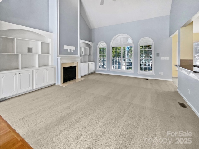 unfurnished living room featuring baseboards, visible vents, a premium fireplace, carpet flooring, and high vaulted ceiling