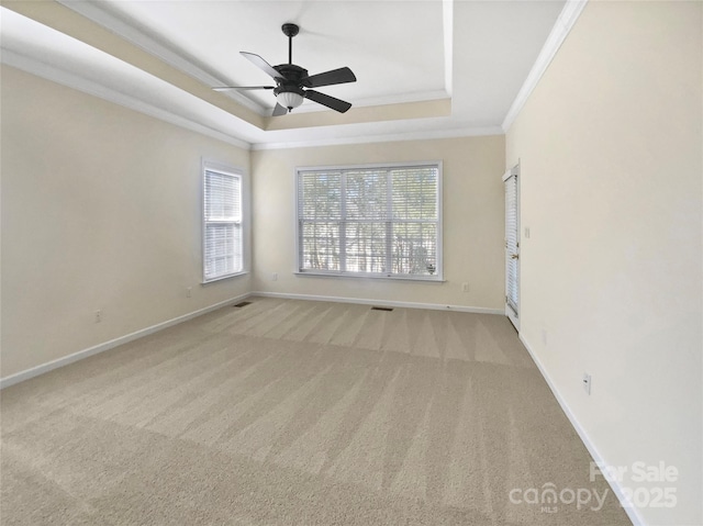 carpeted spare room with a ceiling fan, baseboards, visible vents, a tray ceiling, and crown molding