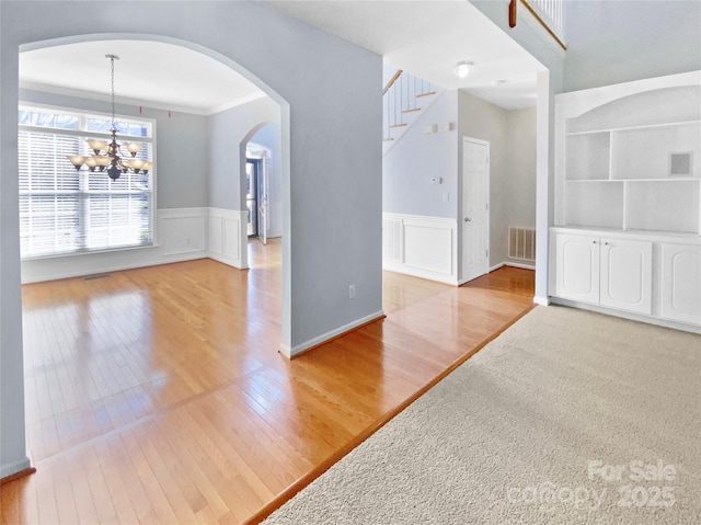 interior space with a chandelier, arched walkways, light wood-style flooring, a wainscoted wall, and visible vents