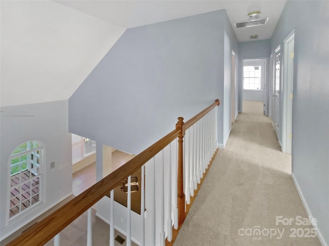 hallway with carpet flooring, an upstairs landing, visible vents, vaulted ceiling, and baseboards