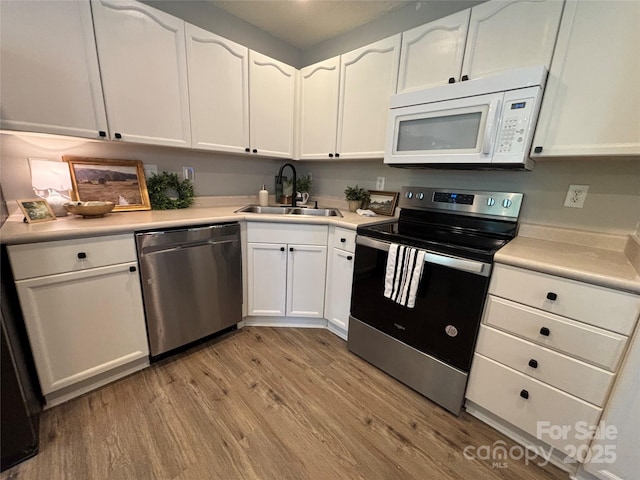 kitchen featuring light wood-style flooring, a sink, white cabinets, and appliances with stainless steel finishes