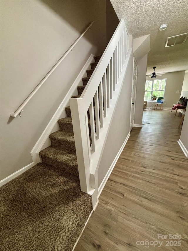 stairway featuring baseboards, wood finished floors, and a textured ceiling