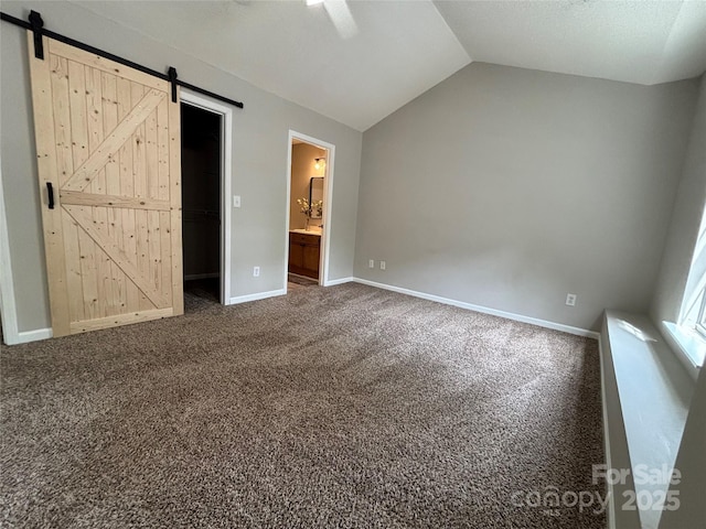 unfurnished bedroom with a barn door, baseboards, vaulted ceiling, carpet, and a walk in closet