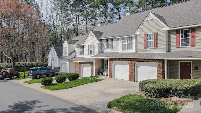 view of property with an attached garage, a chimney, brick siding, and concrete driveway