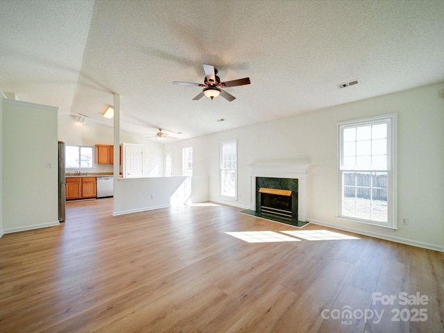 unfurnished living room with lofted ceiling, light wood-type flooring, a premium fireplace, and visible vents