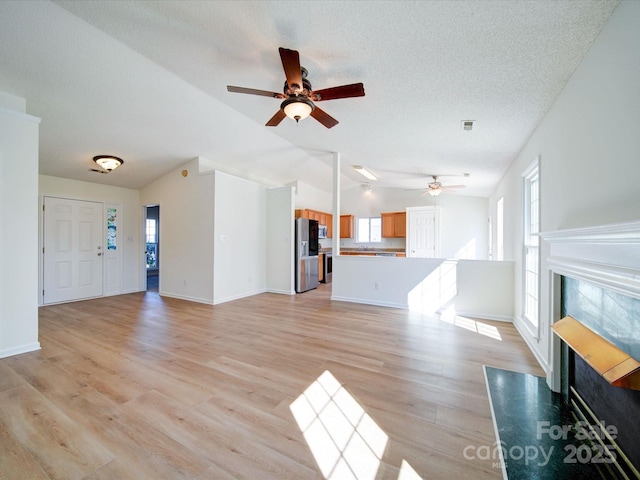 unfurnished living room with baseboards, a tiled fireplace, vaulted ceiling, a textured ceiling, and light wood-type flooring