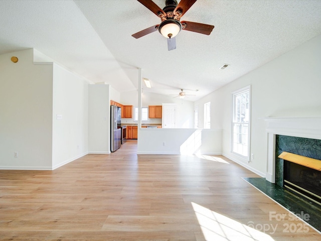 unfurnished living room with lofted ceiling, a textured ceiling, light wood-style flooring, a premium fireplace, and visible vents