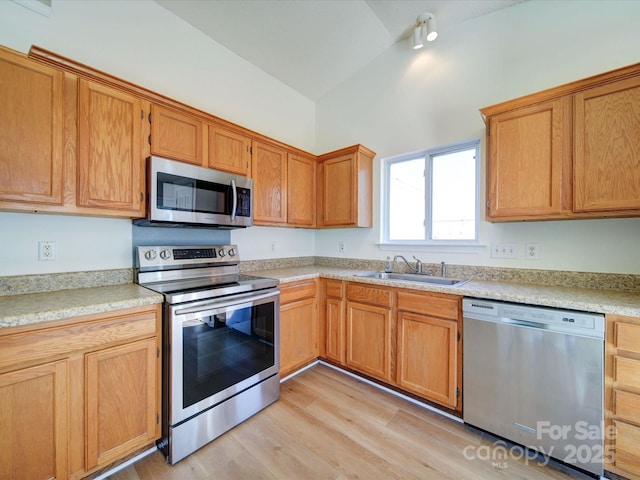 kitchen featuring light wood finished floors, vaulted ceiling, stainless steel appliances, light countertops, and a sink