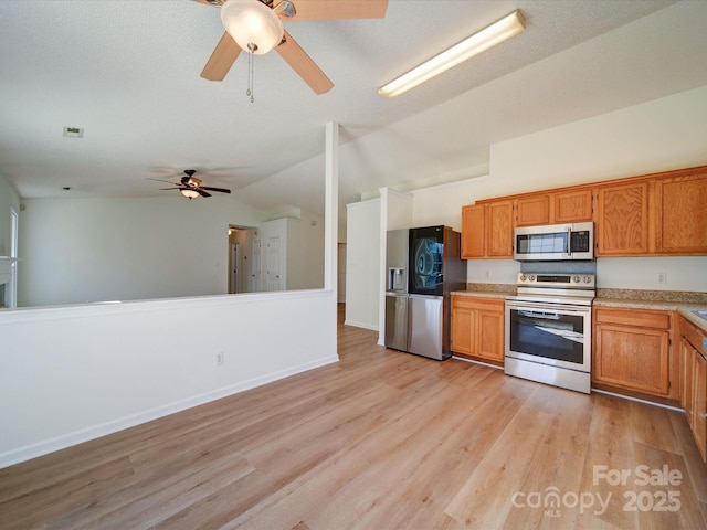 kitchen featuring stainless steel appliances, brown cabinetry, vaulted ceiling, and light wood-style flooring