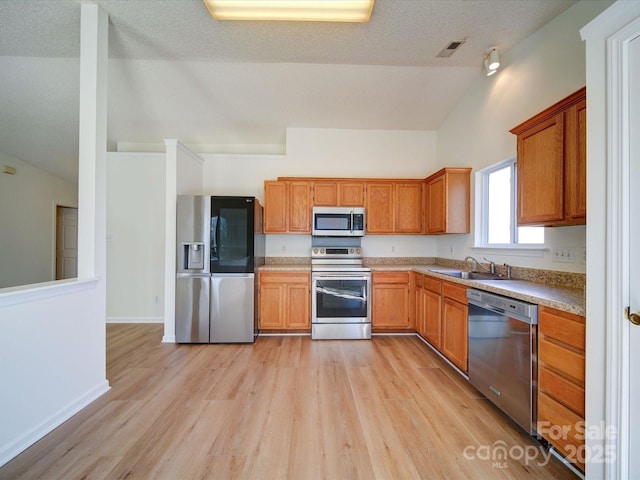 kitchen with a sink, visible vents, light wood-style floors, vaulted ceiling, and appliances with stainless steel finishes