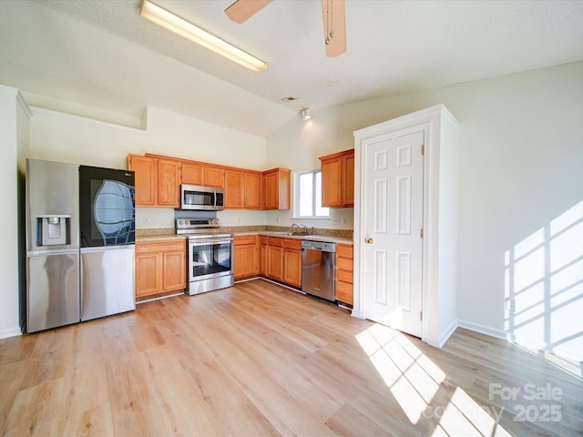 kitchen featuring light wood finished floors, stainless steel appliances, light countertops, vaulted ceiling, and a sink