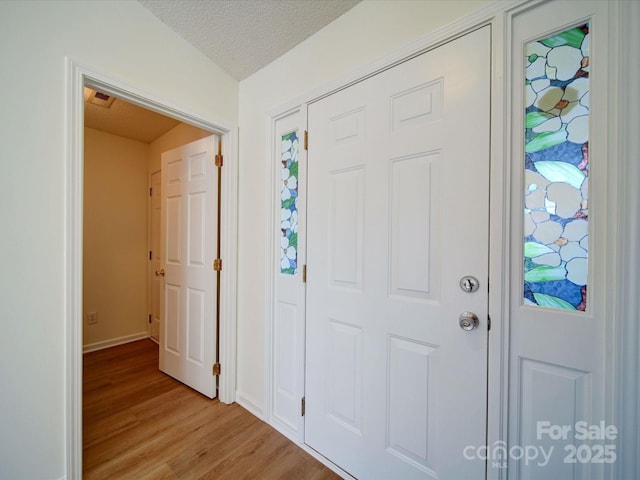 entrance foyer with light wood-type flooring, a textured ceiling, and baseboards