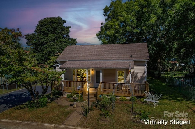 view of front of house featuring a shingled roof, a front yard, covered porch, and fence