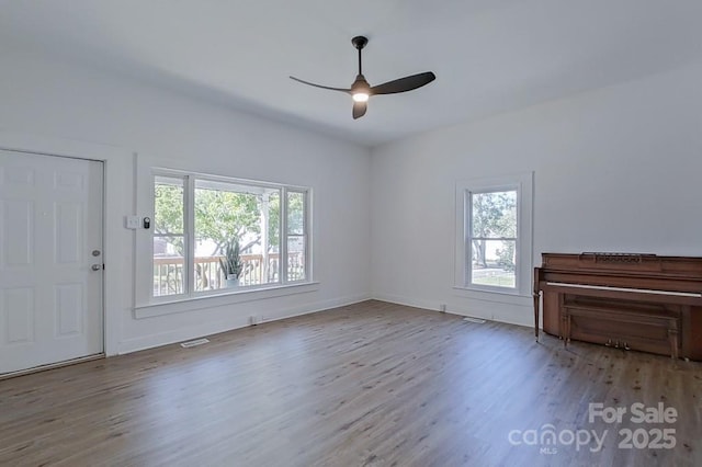 unfurnished living room with a ceiling fan, a wealth of natural light, visible vents, and wood finished floors