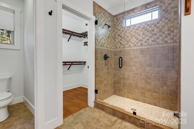 full bath featuring tile patterned flooring, a shower stall, a walk in closet, baseboards, and toilet