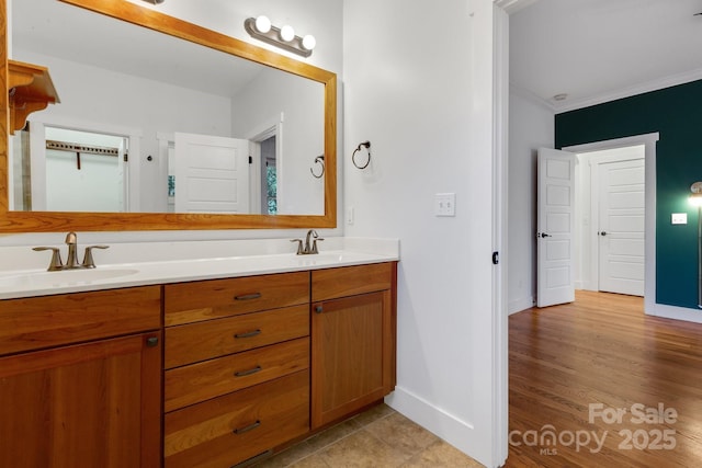 full bathroom featuring double vanity, crown molding, baseboards, and a sink