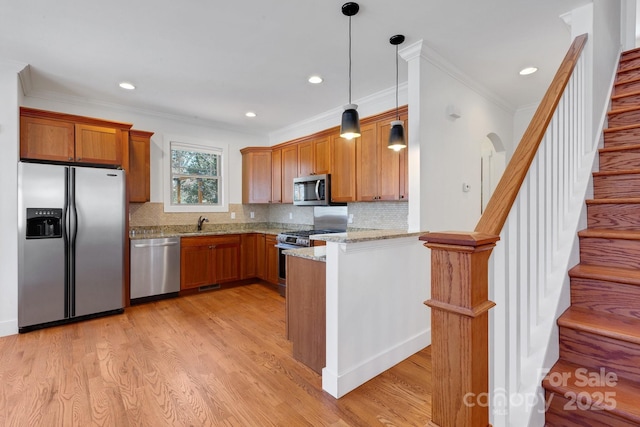 kitchen with pendant lighting, light stone counters, brown cabinets, appliances with stainless steel finishes, and light wood-style floors