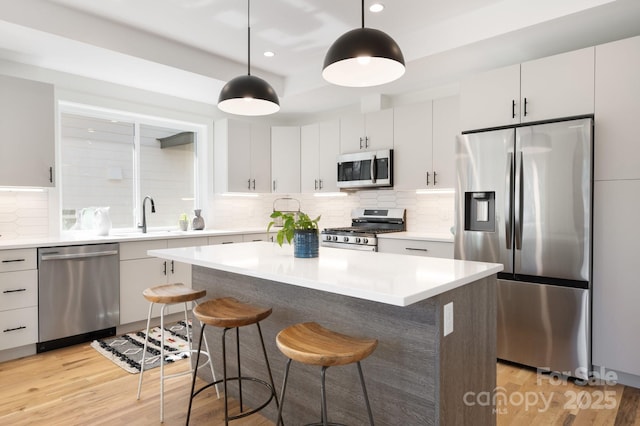 kitchen featuring light wood-style flooring, a sink, appliances with stainless steel finishes, backsplash, and a kitchen bar