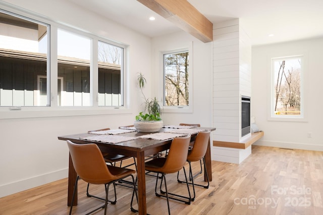 dining space with light wood-style floors, a fireplace, baseboards, and beam ceiling