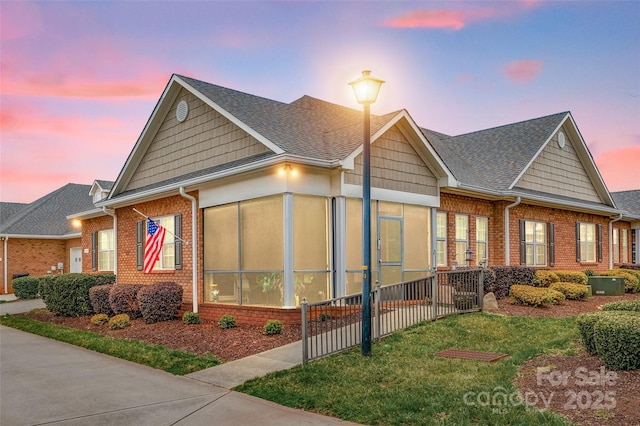 view of front facade with a front lawn, brick siding, a sunroom, and roof with shingles